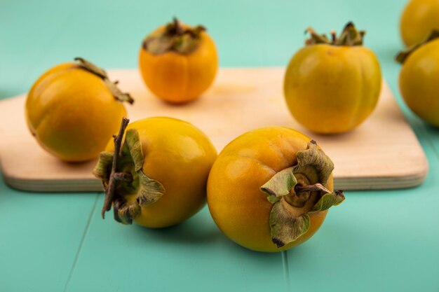 Close up view of unripe persimmon fruits on a wooden kitchen board on a blue wooden wall