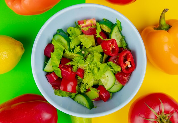 Close-up view of vegetable salad in bowl with pepper tomato lemon on green and yellow background