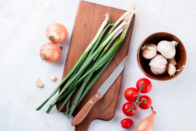 Close-up view of vegetables as onion garlic tomato with cutting board and knife on white background with copy space