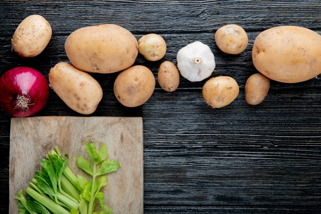 Close up view of vegetables as onion potato garlic with cut celery on cutting board on wooden background with copy space