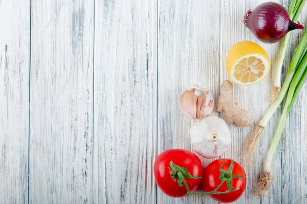 Close up view of vegetables as onion scallion ginger garlic tomato with lemon on wooden background with copy space