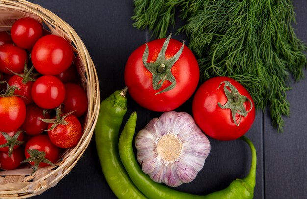 Close up view of vegetables as peppers, garlic, dill and tomato in basket and on black wall