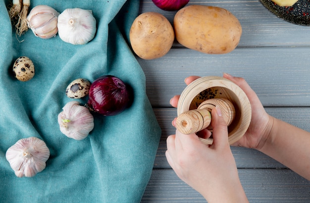 Free photo close up view of vegetables as potato garlic egg onion with woman hand pressing black pepper grains in crusher on wooden background