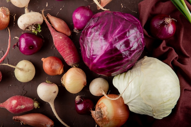 Close-up view of vegetables as purple and white cabbages radish onion on maroon background