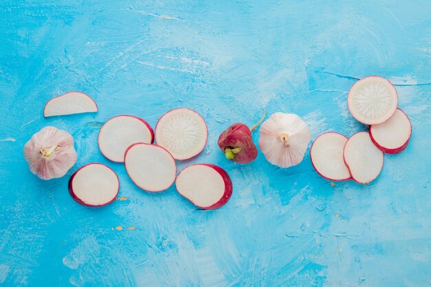 Close-up view of vegetables as whole and sliced radish and garlic on blue background with copy space