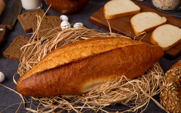 Close-up view of vietnamese baguette on straw surface with different breads on maroon background