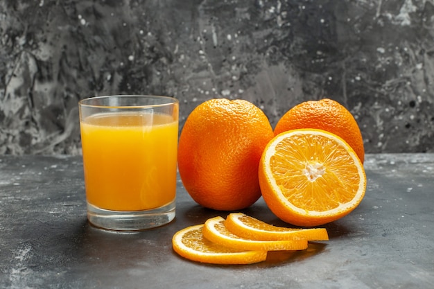 회색 배경에 잘게 잘린 신선한 오렌지와 전체 신선한 오렌지를 자른 비타민 소스의 클로즈업 보기