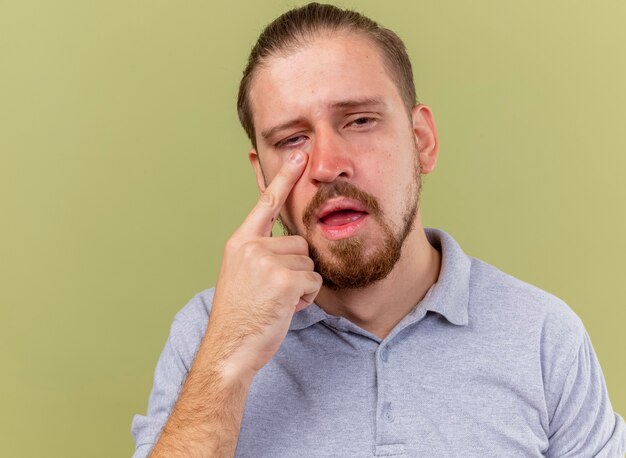 Close-up view of weak young handsome ill man putting finger under eye looking at front isolated on olive green wall