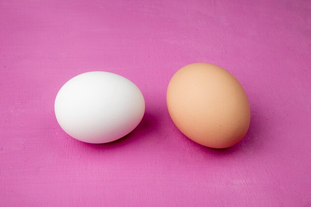 Close-up view of white and brown eggs on purple background with copy space