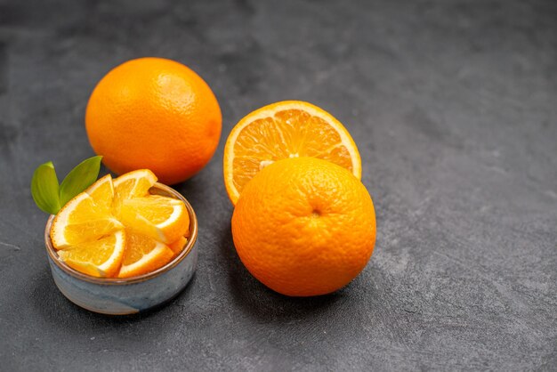 Close up view of whole and chopped fresh oranges on dark table