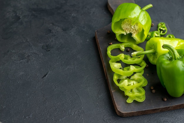 Close up view of whole cut chopped green peppers on dark color wooden cutting board on the left side on black surface