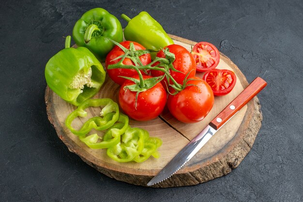 Close up view of whole cut chopped green peppers and fresh tomatoes knife on wooden cutting board on black surface