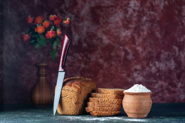 Close up view of whole cut dietary black bread and knife flour in bowl flower pot on blue maroon colors background