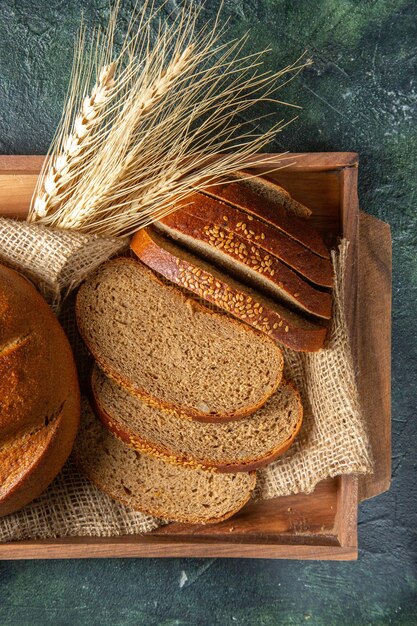 Close up view of whole and cut fresh black bread on towel in a brown wooden box potteries spices on dark mix colors surface