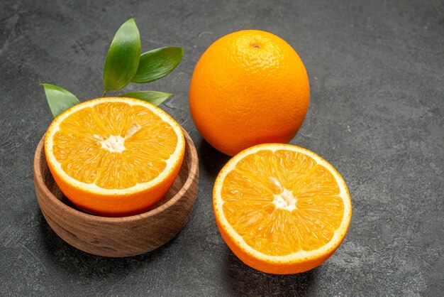 Close up view of whole and cut fresh oranges with leaves on dark table