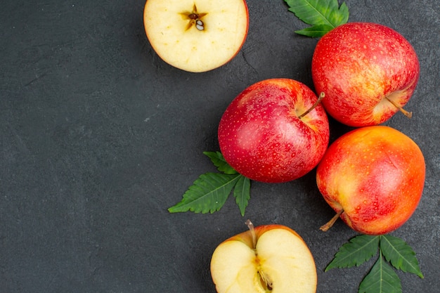 Close up view of whole and cut fresh red apples and leaves on black background