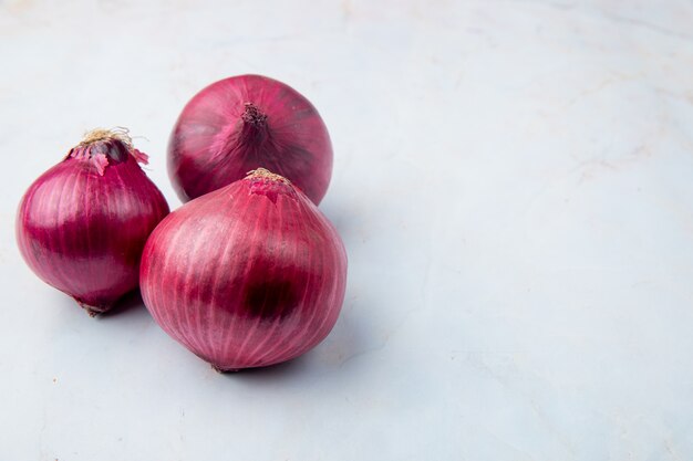 Close-up view of whole red onions on left side and white background with copy space