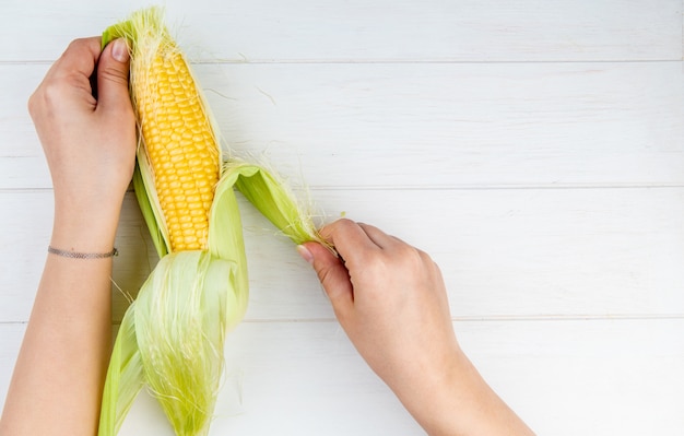 Close-up view of woman hands cleaning corn cob on wooden surface with copy space