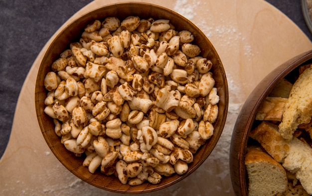 Close-up view of wooden bowl with corns on wooden surface and maroon background