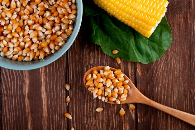 Close-up view of wooden spoon full of dried corn seeds with cooked corn and spinach on wooden surface