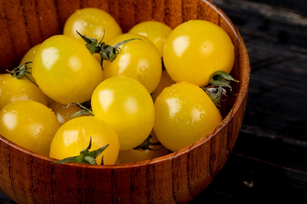 Close-up view of yellow tomatoes in bowl on wooden surface