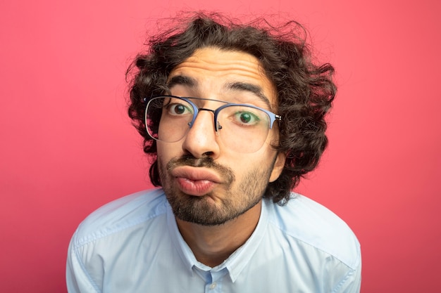 Close-up view of young handsome caucasian man wearing glasses  doing kiss gesture isolated on crimson wall