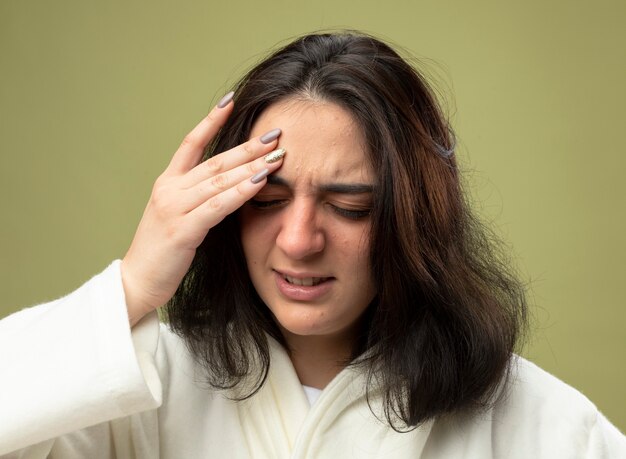 Close-up view of young ill woman wearing robe isolated on olive green wall