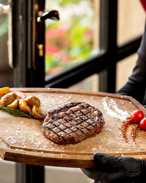 Close up of waiter holding grilled steak served with roasted potato