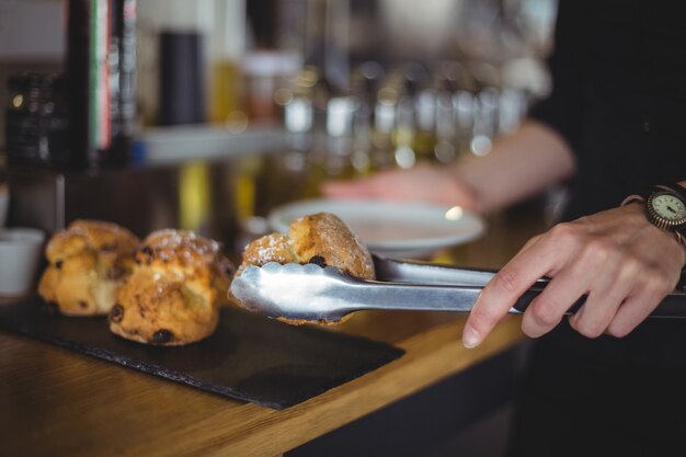 Close-up of waitress serving muffin in a plate at counter