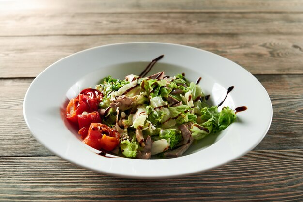 닭고기, 파프리카, 양상추 잎 가벼운 여름 야채 샐러드와 함께 제공되는 나무 테이블에 흰색 그릇의 클로즈업. 맛있고 맛있어 보입니다.