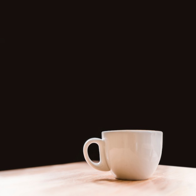 Close-up of white coffee cup on desk over black backdrop