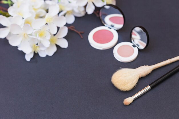 Close-up of white flowers; blusher and makeup brush on gray background