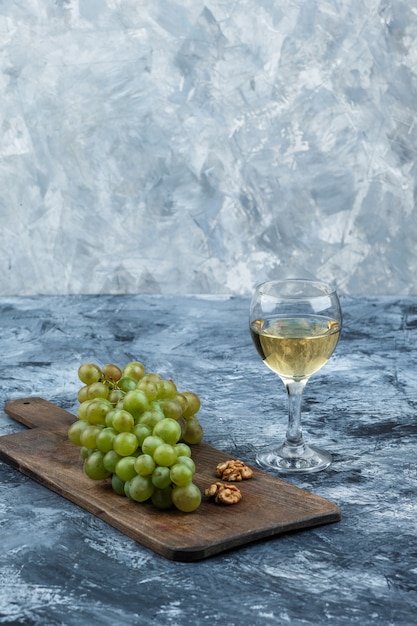 Крупным планом белый виноград, грецкие орехи на разделочной доске со стаканом виски на темно-синем мраморном фоне. вертикальный