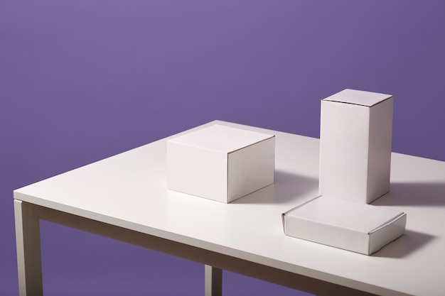 Close up of white paper carton boxes on table isolated over lilac, three blank cases on desk