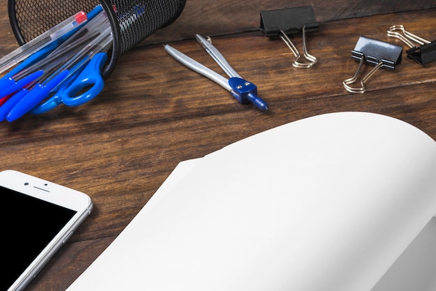 Close-up of white paper with stationeries and cellphone on wooden background