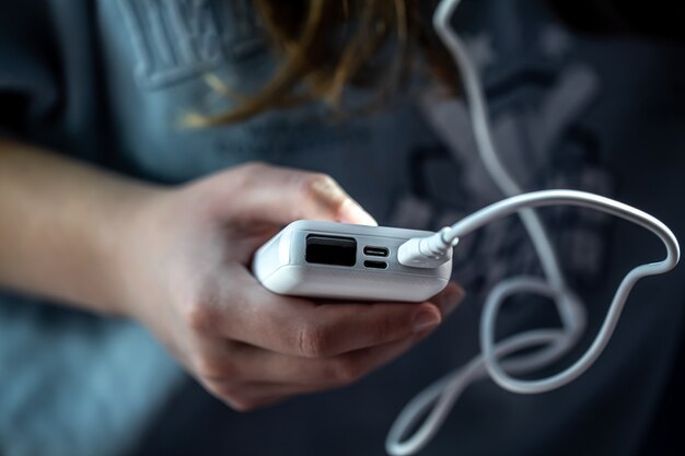 Close-up of a white power bank in a female hand, blurred background.