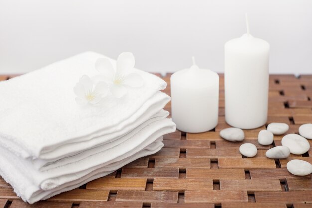 Close-up of white towel; flowers; candles and pebbles on wooden table