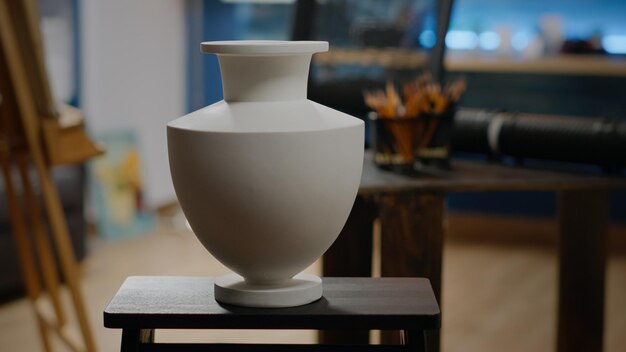 Close up of white vase on table in artwork studio at home with nobody in room but artistic equipment, instruments and art tools. Empty creativity space for professional artist and drawing