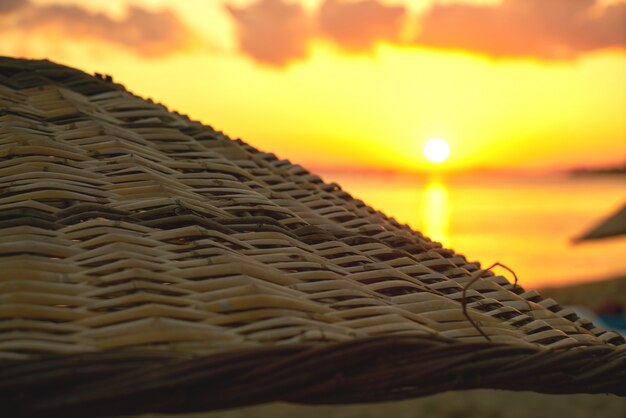 Close-up of wicker parasol with sun background