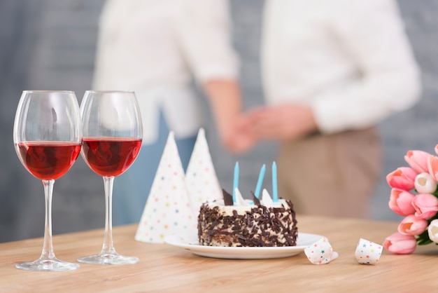 와인 잔의 근접; 맛있는 케이크; 나무 책상에 파티 경적 및 튤립 꽃