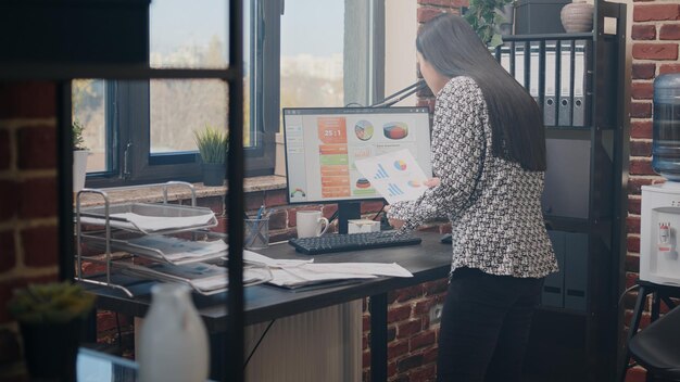 Close up of woman analyzing charts documents on desk to plan business project and strategy. Entrepreneur doing annual analysis with papers and computer to work on startup development.