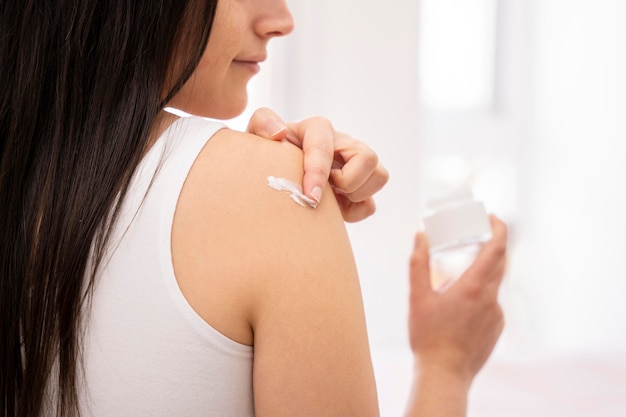 Close-up woman applying cream on shoulder