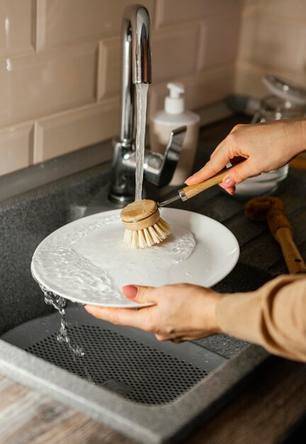 Close up woman cleaning plate with brush