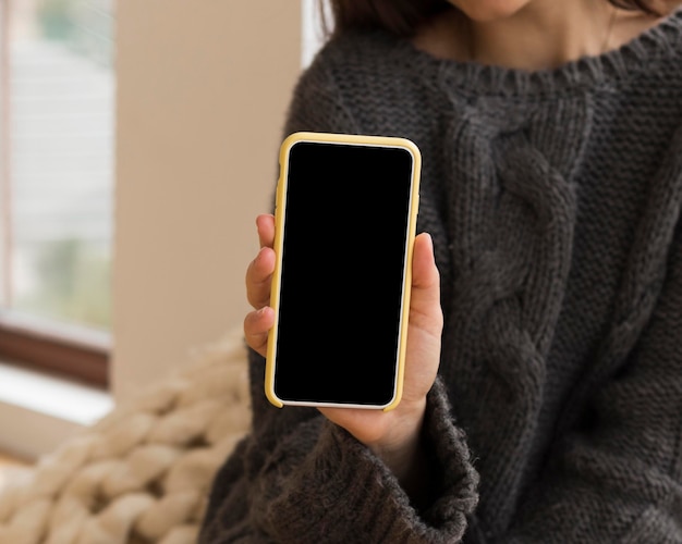 Close-up woman in cozy clothes holding nlank phone