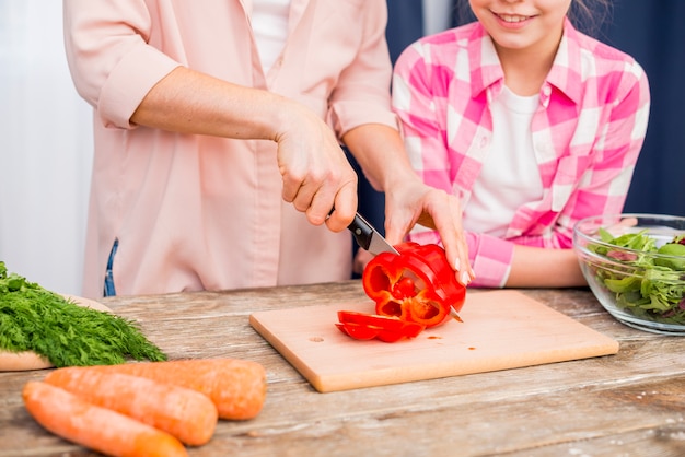 Close-up of woman cutting the bell pepper with knife on chopping board with her daughter