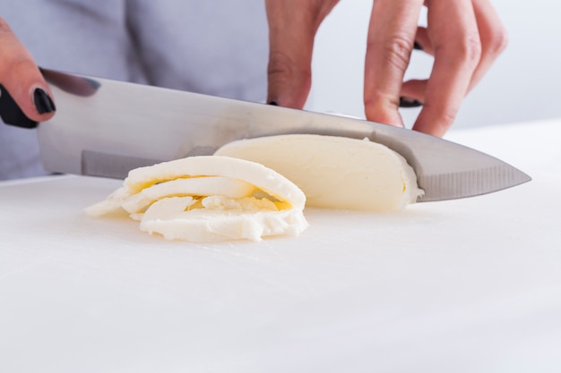 Close-up of a woman cutting the cheese with knife on white table