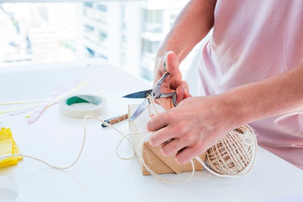 Close-up of a woman cutting the thread from spool with scissor on white table