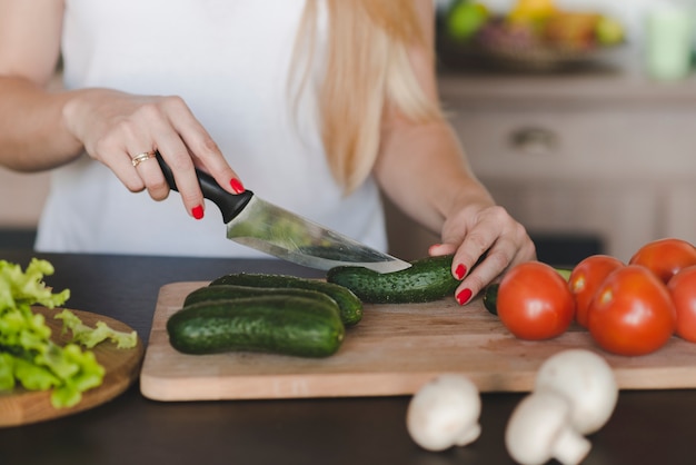 Close-up of woman cutting vegetable with sharp knife on chopping board