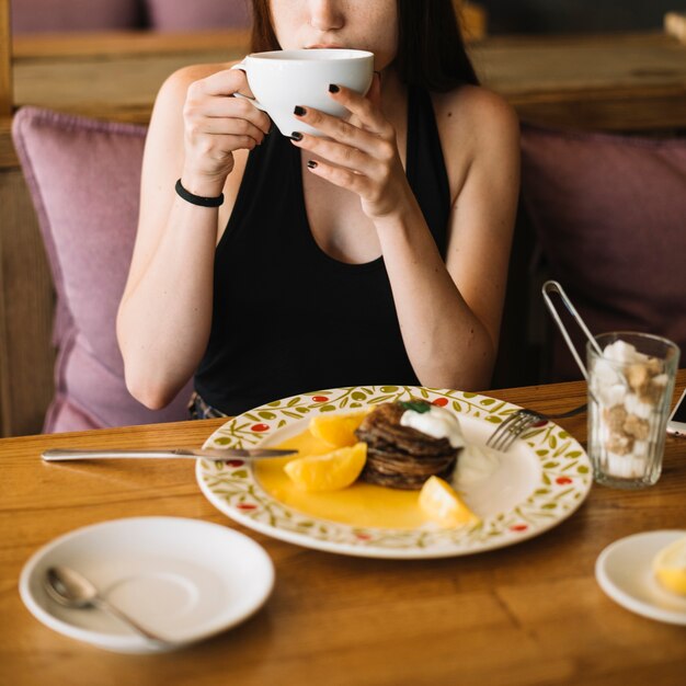 Крупным планом женщина, пить кофе с десертом на тарелке