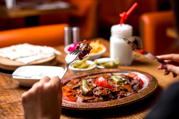 Close up of woman eating iskender kebab in copper platter with pickles yogurt and ayran